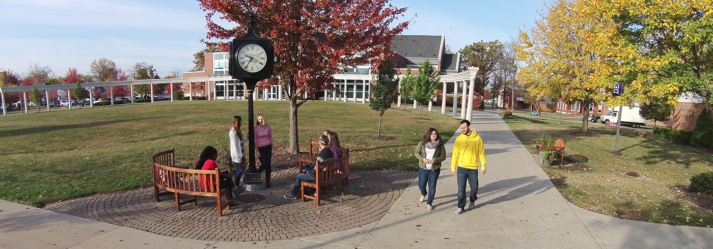 wide campus picture with students talking by the clock and walking on the sidewalk
